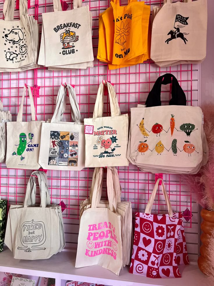 Variety of handmade tote bags displayed on a pink grid wall